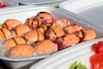 Baked sushi rolls with salmon, cheese and sauce on a foamed polystyrene tray.