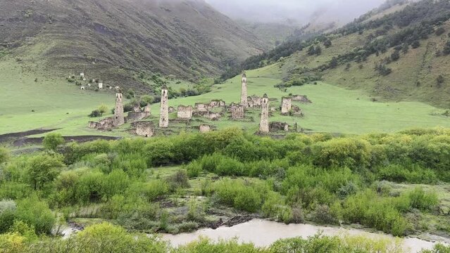 View of the medieval Targim tower complex in the Caucasus mountains surrounded by greenery. The Caucasus Mountains on a cloudy day in Ingushetia. Russia, 4K.