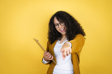 African american business woman with paperwork in hands over yellow background laughing at you, pointing finger to the camera with hand over body, shame expression