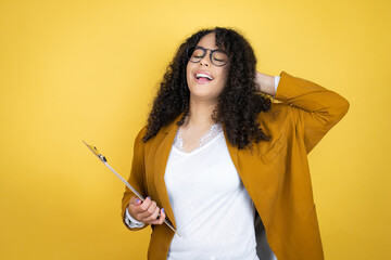 African american business woman with paperwork in hands over yellow background relaxing and stretching, arms and hands behind head and neck smiling happy