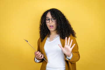 African american business woman with paperwork in hands over yellow background afraid and terrified with fear expression stop gesture with hands, shouting in shock. Panic concept.