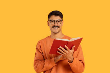 Smiling man with glasses reading a red book