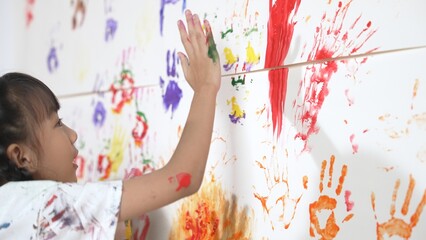 Close up of colorful stained wall was painted by student in art class. Funny asian girl playing with colorful watercolor with diverse children at messy room. Creative activity concept. Erudition.
