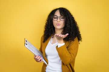 African american business woman with paperwork in hands over yellow background looking at the camera blowing a kiss with hand on air being lovely and sexy. Love expression.