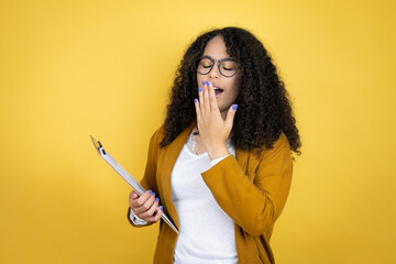 African american business woman with paperwork in hands over yellow background bored yawning tired covering mouth with hand. Restless and sleepiness.