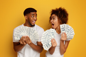 Excited african american couple holding bunch of money banknotes