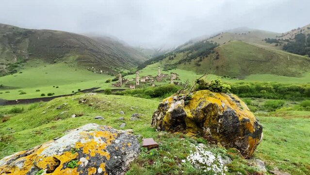 View of the medieval Targim tower complex in the Caucasus mountains surrounded by greenery. The Caucasus Mountains on a cloudy day in Ingushetia. Russia, 4K.
