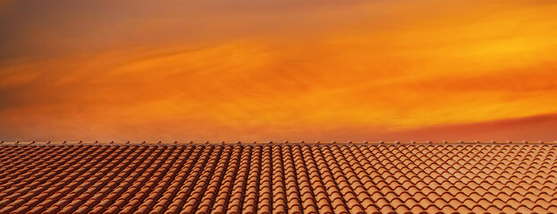 Clay tile roof with bright orange sunset sky in the background. Orange banner with clay tile roof and orange sky, free space for text, copy space