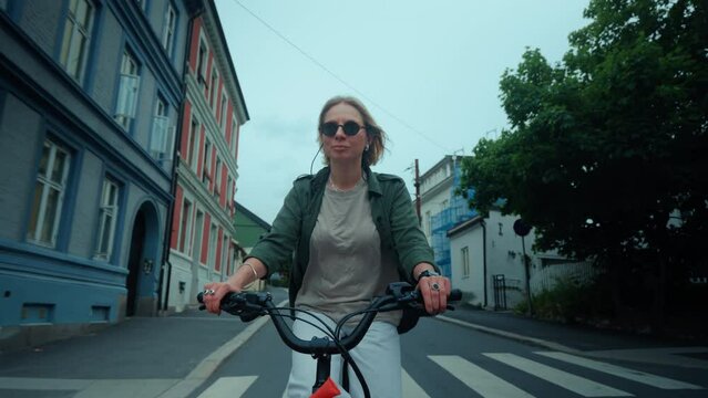 Slow motion shot of happy and stylish young woman cruise around city on commuter bicycle, relaxed handlebar and front rack. Commuting on bike in summer. Happy smiling cyclist 