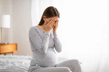 Sad pregnant woman sitting on bed covering face