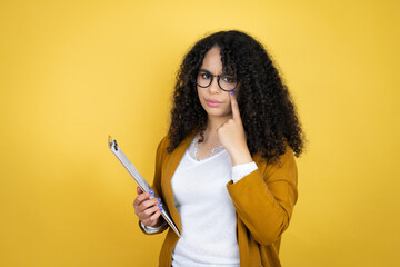 African american business woman with paperwork in hands over yellow background Pointing to the eye watching you gesture, suspicious expression