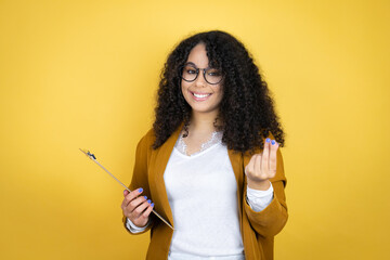 African american business woman with paperwork in hands over yellow background doing money gesture...