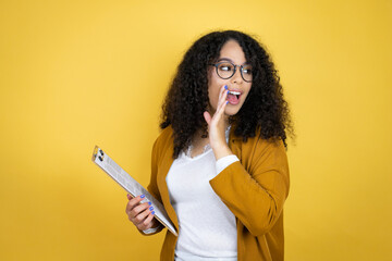 African american business woman with paperwork in hands over yellow background hand on mouth telling secret rumor, whispering malicious talk conversation