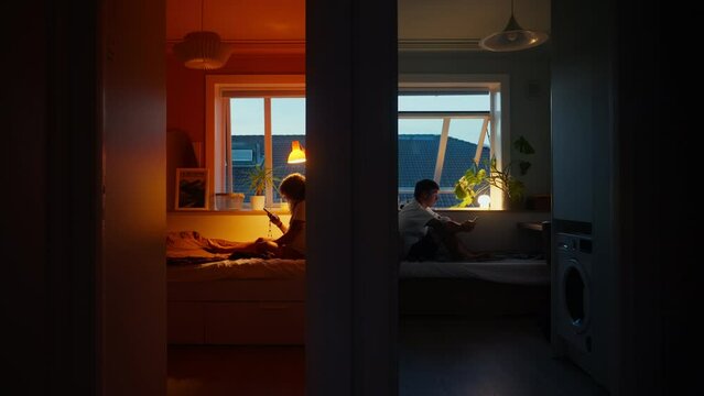 Wide dark shot, color block separated, couple sit in different rooms of apartment. Man and woman use phones, angry with each other, after argument, modern relationship struggle. Cinematic relationship