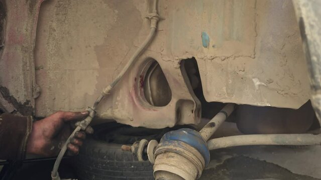 The calloused hands of hillbilly mechanic hitting driveshaft with a hammer during DIY car repairs. Closeup.