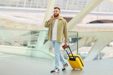 Fototapeta na wymiar Man Walking With Luggage and Talking on Phone at Airport