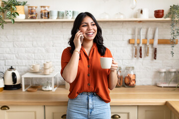 Woman chatting on phone with coffee in kitchen