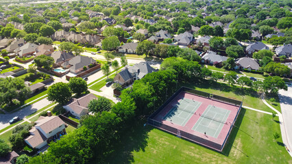 Community tennis courts with chain link fence and players in upscale residential neighborhood with large two-story single-family house, swimming pool, fenced backyard, suburb Dallas, TX, aerial - Powered by Adobe