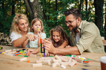Fun family making tower of wooden blocks at picnic table in nature.