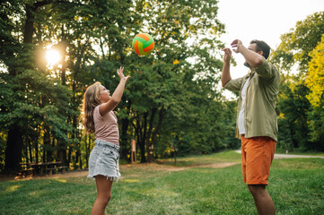 Father and daughter standing on a meadow and playing volleyball.