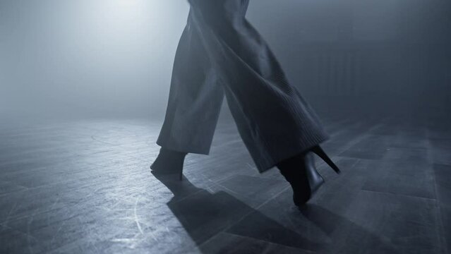 Elegant female heels dancer at smoky stage with spotlights. Close up of woman legs entering stage. Silhouette of dancer legs walking through smoke in dark studio. Tracking shot in 4K, UHD