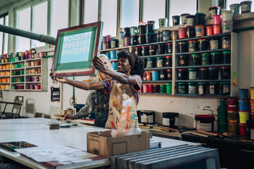 Interracial printing shop workers checking out silk screen frame.