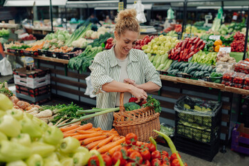 Happy woman putting fresh veggies into a basket at greengrocery market