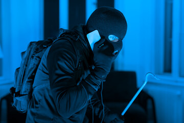 Burglar with phone and crowbar at night