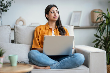 Confident young woman working with her laptop while sitting on a couch at home