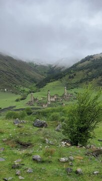 View of the medieval Targim tower complex in the Caucasus mountains surrounded by greenery. The Caucasus Mountains on a cloudy day in Ingushetia. Russia, 4K.