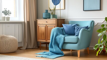 Wooden cupboard next to turquoise armchair in living room interior with blue blanket on sofa