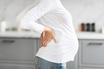 Pregnant woman touches her back gently, cropped