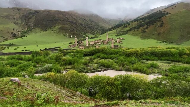 View of the medieval Targim tower complex in the Caucasus mountains surrounded by greenery. The Caucasus Mountains on a cloudy day in Ingushetia. Russia, 4K.