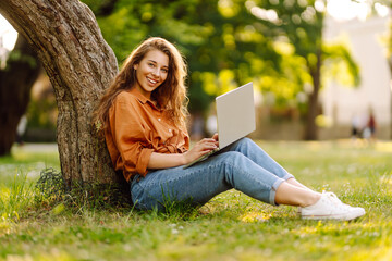 Happy woman with curly hair with a laptop outdoor.  Online education, Freelance work, technology concept.