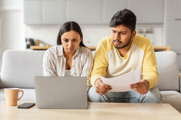 Worried couple with laptop discussing finances at home