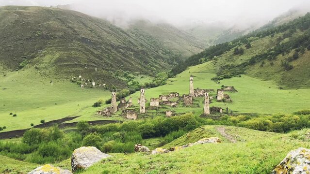 View of the medieval Targim tower complex in the Caucasus mountains surrounded by greenery. The Caucasus Mountains on a cloudy day in Ingushetia. Russia, 4K.
