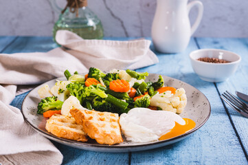 Mix of boiled vegetables, poached egg and waffle toast on a plate on the table