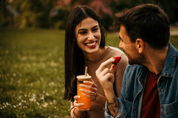 Couple blissfully engaged in a picnic in the countryside and drinking fresh orange juices