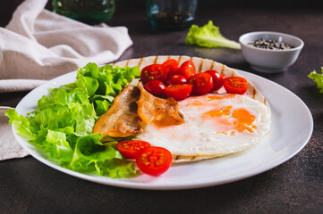 Appetizing tacos with fried egg, bacon, tomato and lettuce on a plate on the table