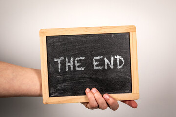 THE END. Chalk board with text in hand on white background - 784773781