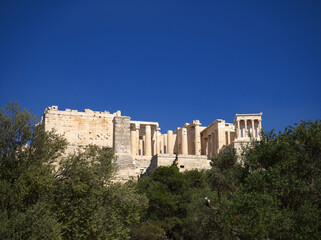 Fototapeta na wymiar Acropolis propylaea gate under blue sky. Groups of olive trees in the foreground. 