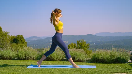 Poster Fit young woman practicing a crescent lunge yoga pose in beautiful sunny garden © helivideo