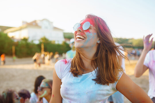 Happy woman covered in rainbow colored powder celebrating holi color festival. Young woman having fun with colorful powder outdoors. Beach party. Traditional Indian holiday.
