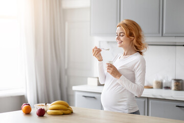 Pregnant lady eating yogurt in the kitchen