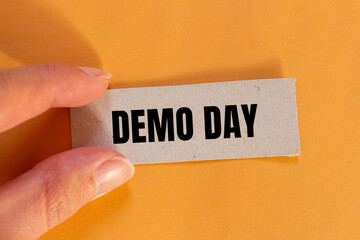 Demo day words written on paper piece with orange background. Conceptual demo day symbol. Copy space.