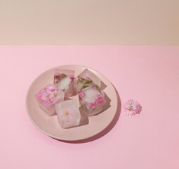 Beautiful small pink flowers in ice cubes on pink plate on beige background, top view