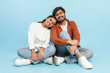 Smiling couple sitting together on floor on blue background