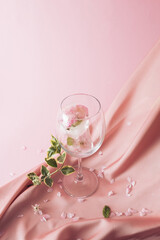 Ice cubes with flowers melting in the drink on a silky pink fabric in the background