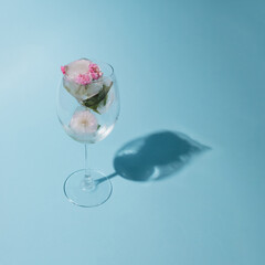 Beautiful small pink flowers in transparent glass on blue background with copy space