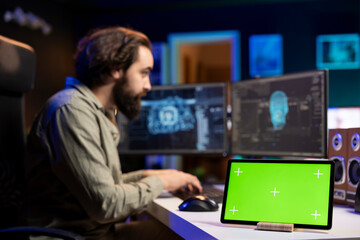 Focus on green screen device next to man in blurry background updating artificial intelligence...